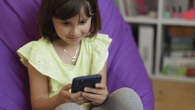 Cute caucasian kid girl holding smart phone enjoying using mobile apps, playing games at home. Small child learning in cellphone, watching video, having fun with mobile technology concept