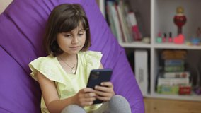 Small child learning in cellphone, watching video, having fun with mobile technology concept. Cute kid girl holding smart phone enjoying using mobile apps, playing games at home
