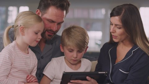 Family in pyjamas having fun sitting on sofa using digital tablet together - shot in slow motion
