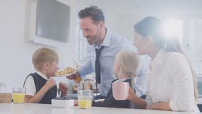 Medium shot of two children wearing school uniform in kitchen eating breakfast waffles as parents get ready for work - shot in slow motion - Powered by Shutterstock - Get 15% off with code: PIKWIZARD15