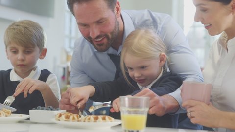 Close up of two children wearing school uniform in kitchen eating breakfast waffles as parents get ready for work - shot in slow motion
