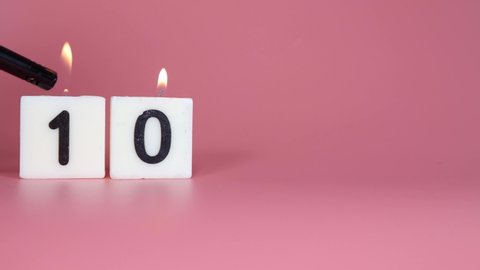 A square candle saying the number 10 being lit and blown out on a pink background celebrating a birthday or anniversary 