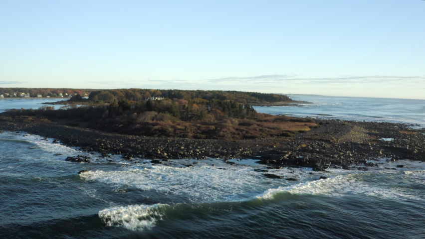 Aerial Rising Above A Small Rocky Island Off The New England Coast, With Crashing Waves, Clear Blue Sky, And The Mainland Shore In The Background - Kennebunkport, Maine