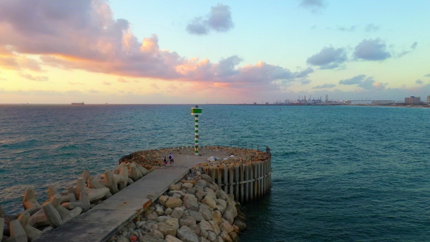 Aerial Shot Of People On Walkway At Groyne By Beautiful Sea Against Sky During Sunset, Drone Panning Over Ocean - Ashdod, Israel