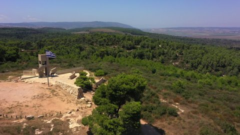 Aerial Shot Of Tourists Exploring Structure By Israeli Flag, Drone Flying Forward Over Green Forest On Sunny Day - Megiddo, Israel