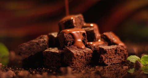 Pouring chocolate sauce on a chocolate brownie dessert. Close up of biscuit cake. Shot in slow motion with RED camera..