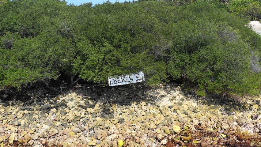 Aerial Panning A Sign On A Rocky Shoreline With Shrubs And Brush Under A Bright Sun - Thulusdhoo, Maldives