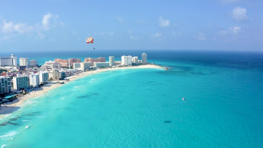 Aerial view of Cancun, Mexico showing luxury resorts and blue turquoise beach. People parasailing, swimming and tanning on the beach. Background of wonderful Caribbean beach in Cancun