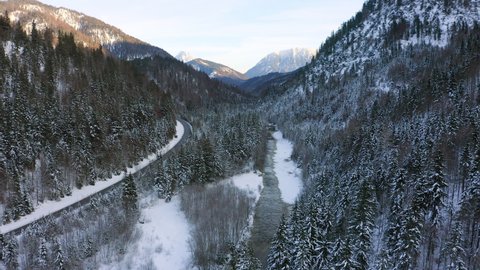 Aerial Panning A River And A Rural Road As It Winds Through A Snowy Alpine Valley, With Soaring Pine Trees And Steep Mountain Hillsides - Bavaria, Germany