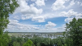 4k stock video timelapse of beautiful sunny morning scenic landscape of flooded countryside area as seen from high hill. White fluffy clouds flying over horizon in blue sky over green trees and river