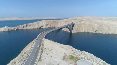 Aerial tilt down shot of a car driving across a bridge over the ocean on the beautiful island of Pag, Croatia