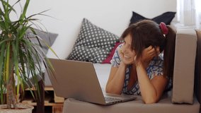 Woman lying on the sofa in an apartment watches a movie or a series on a laptop