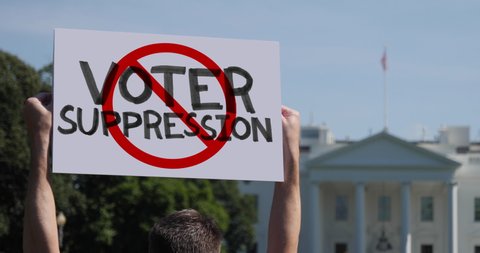 WASHINGTON, DC - Circa March, 2021 - A man waves a handmade STOP VOTER SUPPRESSION protest sign outside the White House.  	