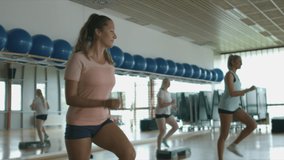 Handheld shot of four smiled Caucasian young women in sportswear using athletic platforms to do step-up exercises in the gym - Powered by Shutterstock - Get 15% off with code: PIKWIZARD15
