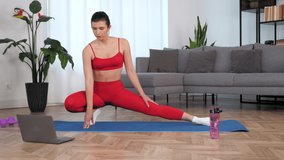 Beautiful fit woman in sportswear study watch online remote sport webinar lesson course master class laptop computer, doing warm-up stretching training workout exercise on yoga or fitness mat at home