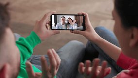 Couple Using video call at home to connect with friends at home. Shot behind models shoulders. Back view of young atractive couple boy and girl sitting at home and speaking online on smartphone.
