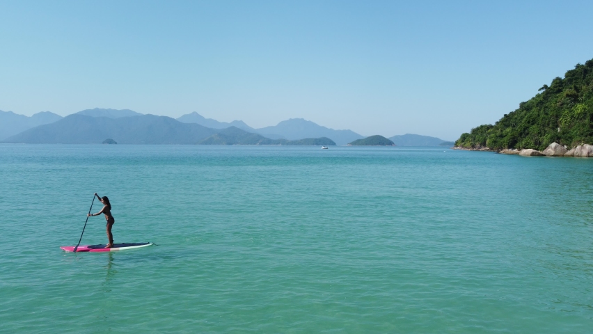 Aerial view of young woman on stand up paddling on vacation, on crystal water tropical island, floating on the reef rocks sea. girl on sup