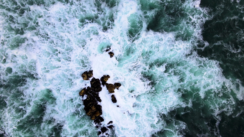 Aerial - Drone rises from rock in ocean, incessant pounding of waves Royalty-Free Stock Footage #1073552978