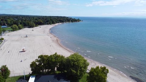 Uncrowded white sandy beach surrounded by trees and clear turquoise blue water; aerial 4k