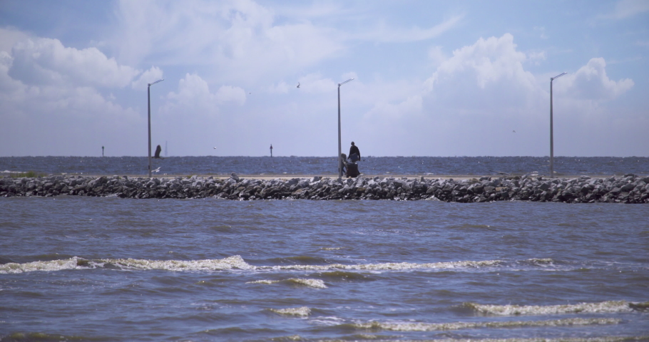 A father and son walk along a stone pier in with fishing gear in hand on a beautiful, sunny day in Gulfport, Mississippi. Filmed in 4K 