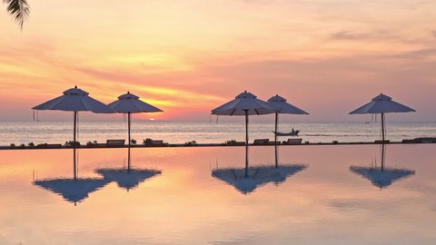 A dramatic orange, yellow and pink sunset reflects in the still waters of a resort swimming pool. Video Stok