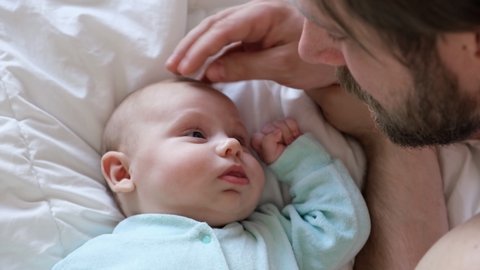 Dad touching and stroking a tiny infant. Newborn baby smiling and looking up at him. Fatherhood concept with daddy showing affection to baby. Authentic video of beard Father caressing his newborn baby