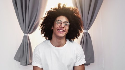 Happy man portrait. Skincare grooming. Positive lifestyle. Cheerful satisfied handsome guy with long curly hair in white t-shirt eyeglasses smiling looking at camera in light room.