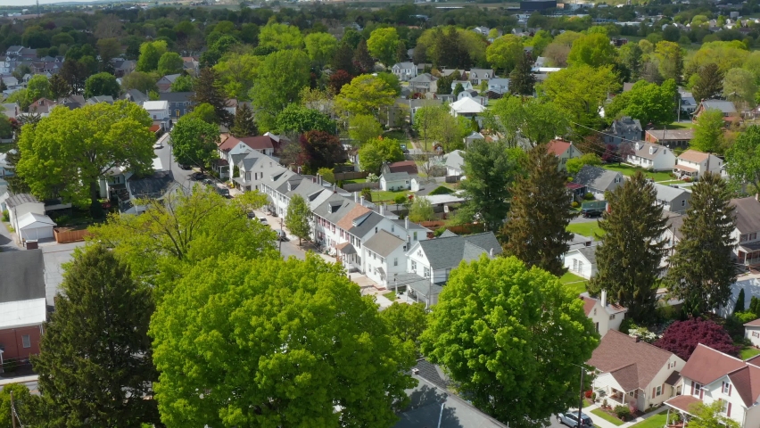 Traditional 1900s homes line street in suburbs outside America city. Small town America. East Coast USA establishing aerial with green summer trees.
