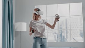 Attractive woman in t-shirt imitates drawing painting at playing videogame with virtual reality headset and joysticks slow motion