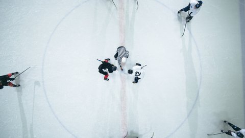 Top View Ice Hockey Rink Arena Game Start: Two Players Face off, Sticks Ready, Referee Drops the Puck, Athletes fight for It. Intense Game Wide of Competition. Aerial Drone Zoom Out Pull Back Shot