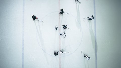 Top View Ice Hockey Rink Arena Game Start: Two Players Face off, Sticks Ready, Referee Drops the Puck, Athletes fight for It. Intense Game Wide of Competition. Aerial Drone Wide Static Shot