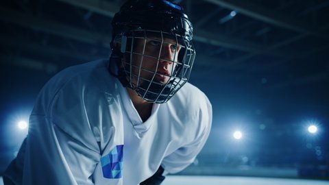 Ice Hockey Rink Arena: Confident Professional Player Ready for Faceoff and Match Start. Portrait of the Young Athlete, Determined to Win Championship, Ready to Hit that Goal. Cinematic Medium Arc Shot