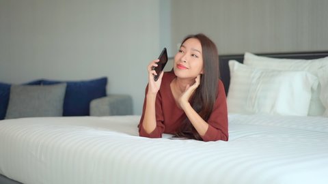 A young woman lying prone on a hotel suite bed talks on her cellphone.