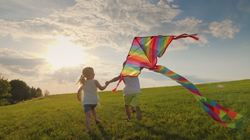 Joyful little children running holding hands and playing with a kite on the meadow in the rays of the sun at sunset Royalty-Free Stock Footage #1073577539