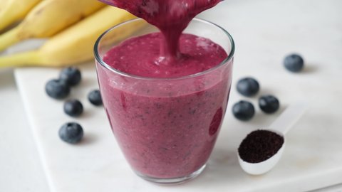 Pouring Acai blueberry and banana smoothie in a glass. Healthy thick smoothie, superfood, summer refreshing drink rich in Vitamins and Antioxidants
