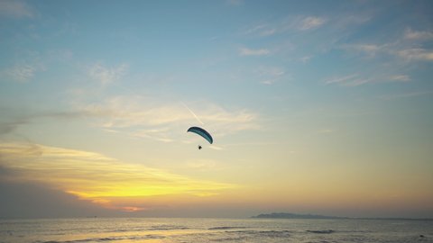 Alone paraglider flying against the colorful sunset, sunrise sky above the sea. Extreme sports, paragliding