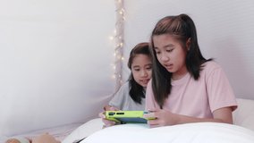 4K Kid play portable game together in bed sheet tent. Two girl sibling happy enjoy and fun to play portable game together. Sibling girl play game in bed sheet tent at home
