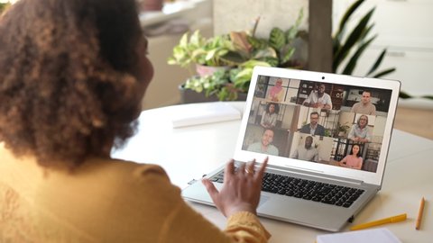Young African-American woman using laptop for remote video connection with group of diverse colleagues, takes a part in virtual meeting, talking and discussing online, engaged in video call