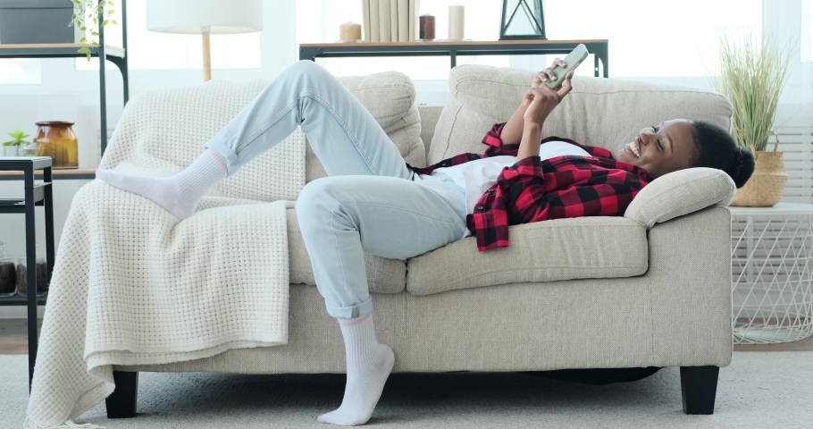 Happy African American woman lying on sofa and using mobile phone