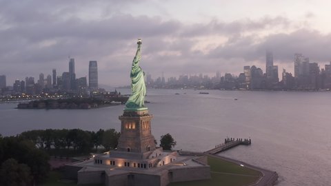 Beautiful Establishing Shot of Statue of Liberty looking towards Manhattan Scenic Skyscraper Skyline covered in Fog in early morning or Sunset, Aerial Orbit Drone Shot