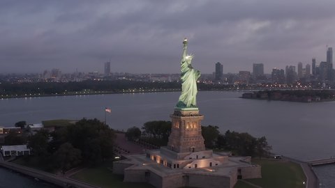 Orbit Drone Shot Around Famous Statue of Liberty revealing Manhattan Scenic Skyscraper Skyline in early Morning Sunrise, Aerial Dolly Slide left