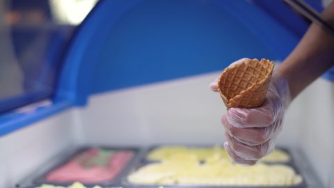 Italian ice cream is placed in a waffle cone from a container in the refrigerator. Close-up of a pastry chef's hands are holding a delicious cone.
