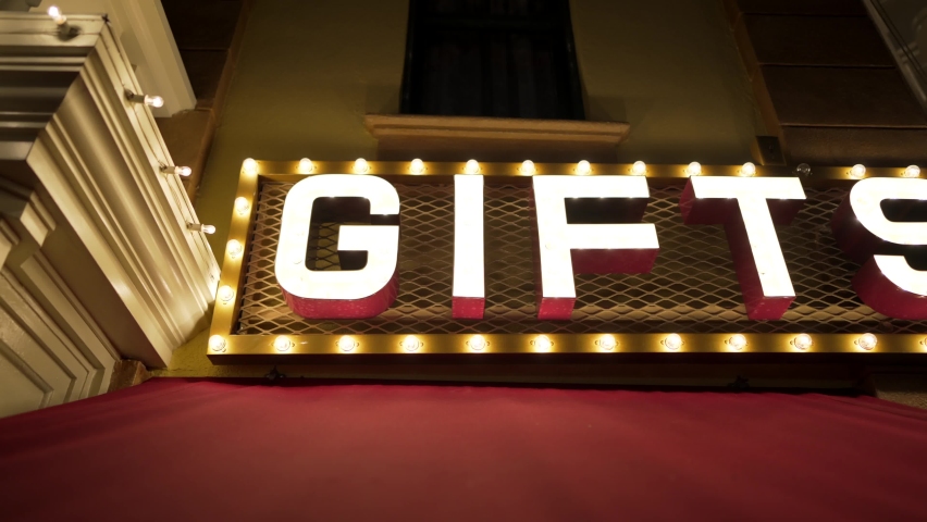 This panning video showcases an old time retro strobing "gifts" sign at night above a red storefront canopy.