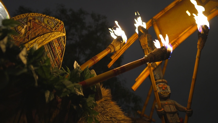 This video shows a row tiki torches held by tiki gods lining the hut of an outdoor Polynesian luau at night. | Shutterstock HD Video #1073592449