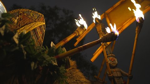 This video shows a row tiki torches held by tiki gods lining the hut of an outdoor Polynesian luau at night.