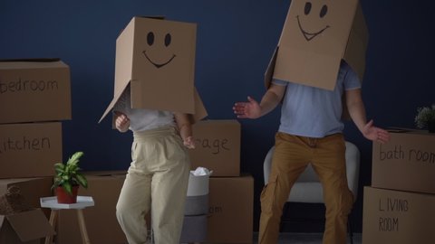 Moving and relocation concept. Packing and decluttering. Unrecognizable couple, husband and wife, dancing with cardboard boxes on their heads, funny video