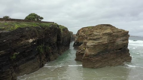 Dangerous drone flight between rocky cliffs at Las Catedrales coast. Aerial backward