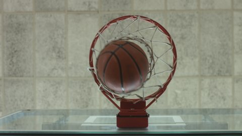 Static shot of a ball hitting the basket backboard, passing through a hoop and shaking the net, low angle view