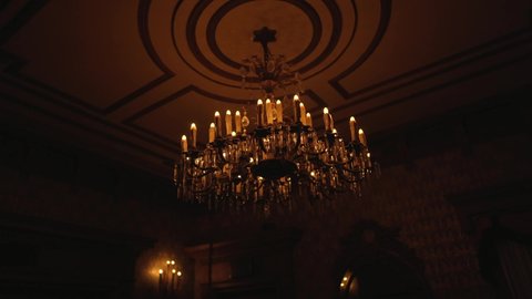 This video showcases a flickering old antique chandelier hanging from the ceiling of a creepy and spooky dark old plantation mansion.