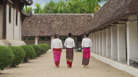 A group of northern Thai young Asian women with traditional Lanna costume holding flowers, walking at Wat Ton Kwen or Wat Inthrawat, Chiang Mai, Thailand. People lifestyle
